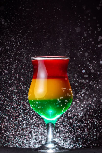 alcoholic cocktail in a glass container on the background of a black wall and drops of water