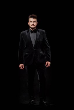 Stüdyoda siyah bir arka planda erkek portresi; siyah bir iş elbisesi giymiş; kameraya bakın.