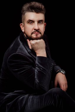 Stüdyoda siyah bir arka planda erkek portresi; siyah bir iş elbisesi giymiş; kameraya bakın.