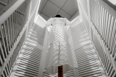 Beyaz bir elbise beyaz bir ekranın arka planında asılı duruyor.