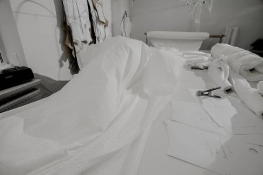 Elbise için kaotik olarak buruşmuş beyaz kumaş masanın üzerinde yatar; elbisenin üretimi için kumaş kesim masasında yatar