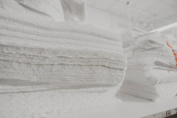Many layers of prepared white fabric for sewing clothes lie on the table; fabric with a fine texture lie in the production warehouse