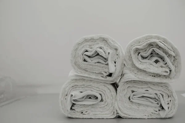 rolls of white fabric for sewing a dress at the factory lie on the table;  rolls of white fabric for sewing a dress at the factory lie on the table; rolls of fabric lie on top of each other against a white wall