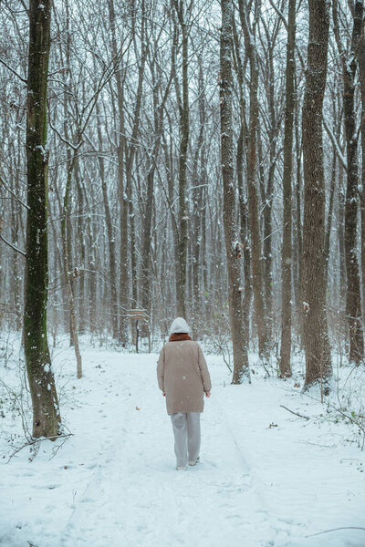 the girl stands in the middle of the forest on the path and looks at the camera; wearing a jacket, a hood from a hoodie and a scarf, wearing sneakers