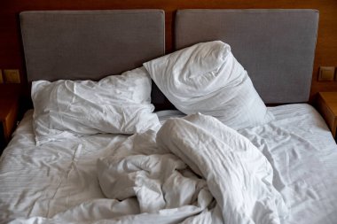 yastıklar ve battaniyeler uygunsuz bir şekilde yatakta uzanır; yatakta yapılmamış yatak; beyaz yatak çarşafları