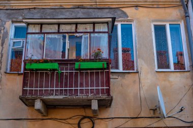 Binanın ön cephesinin bir kısmı ve inşa edildiği malzeme; beyaz pencereli ve uydu antenli bir evde camlı eski bir balkon.