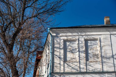 Binanın ön cephesinin bir parçası ve onun inşa edildiği malzeme; mavi gökyüzü arka planında bir ağacın yanında beyaz cepheli eski bir tarihi bina