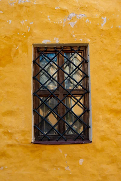Part of the decoration of the facade of the building and the material from which it is built;  a yellow wall with a window behind black bars