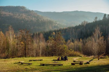 uzay manzaralı sonbahar manzarasının bir parçası; aile dağların ve ormanın arka planına karşı bir bankta oturuyor