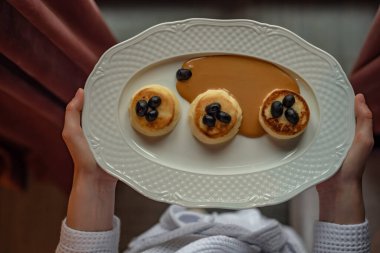 Masada kahvaltılı beyaz tabak; ekşi krema reçelli cheesecakes; kız elinde kahvaltı ile bir tabak tutuyor