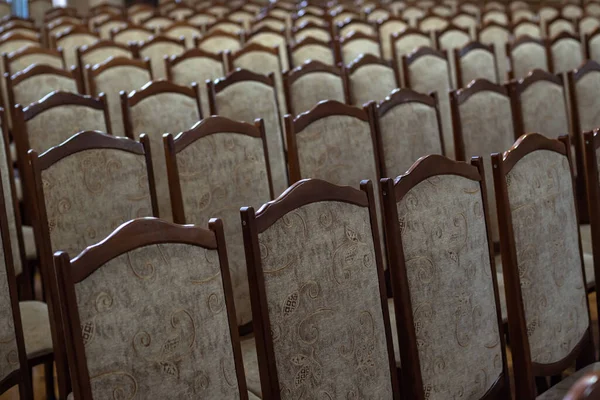 many vintage chairs in the hall with soft upholstery;wooden chairs completely fill the photo