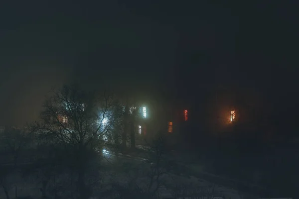 a two-story house in the fog; There are several windows in the house; di m among the trees in a thick fog; night landscape