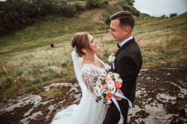 Yeni evliler düğün günlerinde bir fotoğrafçıya doğanın arka planına karşı poz verirler; adam koyu klasik bir ceket giyer ve kadın beyaz bir elbise giyer; çok mutlu ve neşeli bir çift aşık olur.