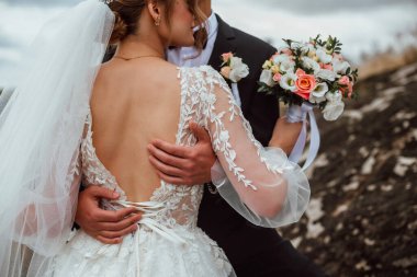 Yeni evliler düğün günlerinde bir fotoğrafçıya doğanın arka planına karşı poz verirler; adam koyu klasik bir ceket giyer ve kadın beyaz bir elbise giyer; çok mutlu ve neşeli bir çift aşık olur.