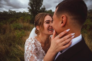 Yeni evliler düğün günlerinde bir fotoğrafçıya doğanın arka planına karşı poz verirler; adam koyu klasik bir ceket giyer ve kadın beyaz bir elbise giyer; çok mutlu ve neşeli bir çift aşık olur.