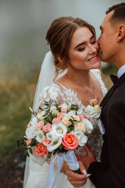 Yeni evliler düğün günlerinde bir fotoğrafçıya doğanın arka planına karşı poz verirler; adam koyu klasik bir ceket giyer ve kadın beyaz bir elbise giyer; çok mutlu ve neşeli bir çift aşık olur.