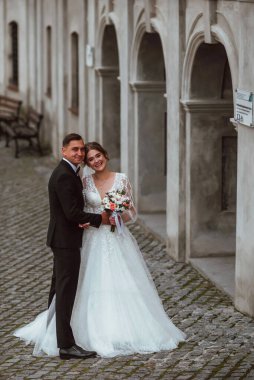 Yeni evliler düğün günlerinde bir fotoğrafçıya doğanın arka planına karşı poz verirler; adam koyu klasik bir ceket giyer ve kadın beyaz bir elbise giyer; çok mutlu ve neşeli bir çift aşık olur.