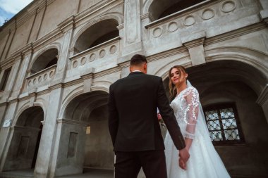 Yeni evliler düğün günlerinde bir fotoğrafçıya doğanın arka planına karşı poz verirler; adam koyu klasik bir ceket giyer ve kadın beyaz bir elbise giyer; çok mutlu ve neşeli bir çift aşık olur.