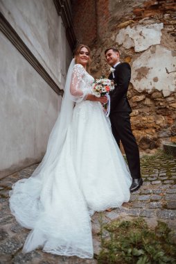 Yeni evliler düğün günlerinde bir fotoğrafçıya doğanın arka planına karşı poz verirler; adam koyu klasik bir ceket giyer ve kadın beyaz bir elbise giyer; çok mutlu ve neşeli bir çift aşık olur.