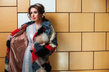 Uzun kürk giyen seksi bir kız içeride duvara karşı poz veriyor.;