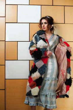 Uzun kürk giyen seksi bir kız içeride duvara karşı poz veriyor.;