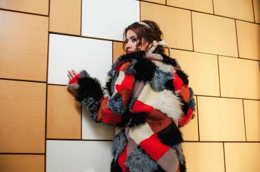 Uzun kürk giyen seksi bir kız içeride duvara karşı poz veriyor.;