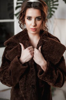 Kürk manto giymiş seksi bir kız ve kapının arkasında poz veriyor; sıcak, uzun kürk manto.