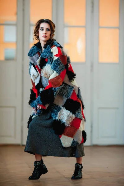 sexy girl dressed in a fur coat and posing indoors on the background of the door; warm long fur coat