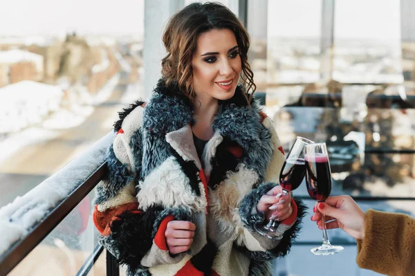 girls dressed in fur coats and drinking red wine; holding a glass of red wine