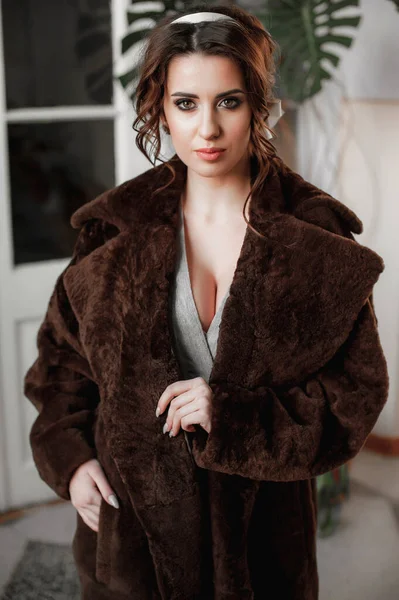 sexy girl dressed in a fur coat and posing indoors on the background of the door; warm long fur coat