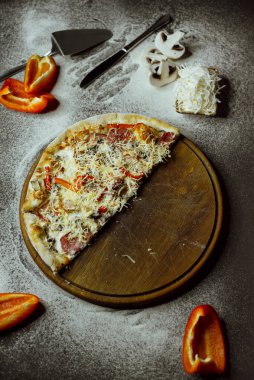 on a black background there is a pizza on a board, scattered flour, pepper, mushrooms and utensils; sliced pizza; not a whole pizza on the board; pieces of pizza on the table