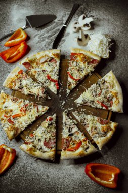 on a black background there is a pizza on a board, scattered flour, pepper, mushrooms and utensils; sliced pizza; not a whole pizza on the board; pieces of pizza on the table