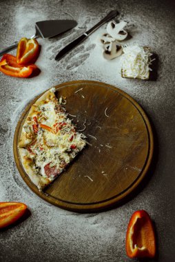 on a black background there is a pizza on a board, scattered flour, pepper, mushrooms and utensils; sliced pizza; not a whole pizza on the board; pieces of pizza on the table