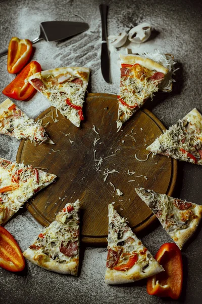 on a black background there is a pizza on a board, scattered flour, pepper, mushrooms and utensils; sliced pizza; not a whole pizza on the board; pieces of pizza on the table