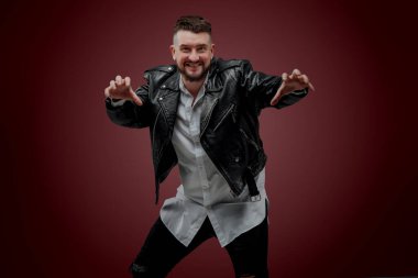 The man is dressed in a Ukrainian shirt; a man in a leather jacket poses on a red background; shows different facial expressions and gestures; poses in sunglasses in the studio; charismatic portrait of a man with a beard