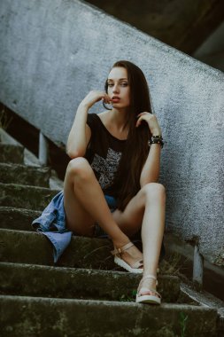 teenage girl with long hair poses; slender figure of a beautiful girl with emotional facial expressions; sunglasses on the head; a person against the background of a city landscape;