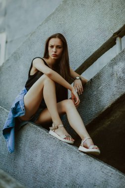teenage girl with long hair poses; slender figure of a beautiful girl with emotional facial expressions; sunglasses on the head; a person against the background of a city landscape;