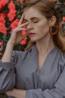 A girl poses in a botanical garden among plants. The model is wearing a gray suit. Freckles on the girl's face. The girl poses among flowers, bushes, trees, cacti.