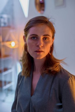 The girl poses in a cafe. The model is wearing a gray suit. Freckles on the girl's face. A fair-haired girl poses in a lit room near a lamp