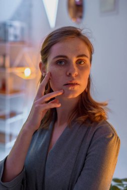 The girl poses in a cafe. The model is wearing a gray suit. Freckles on the girl's face. A fair-haired girl poses in a lit room near a lamp