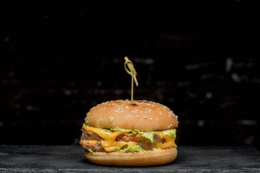 hamburger with a latch on a black board on a dark background. Delicious fast food. A product made by a chef in a cafe