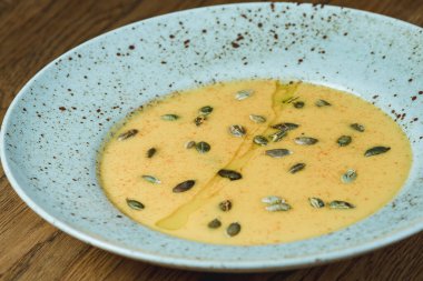 Dishes from the chef of the restaurant. A dish on a table in a cafe. Appetizing food from the restaurant menu. Fresh and tasty food. Pumpkin soup sprinkled with pumpkin seeds in a plate. Seasonal dish