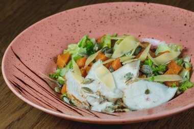 Dishes from the chef of the restaurant. A dish on a table in a cafe. Appetizing food from the restaurant menu. Fresh and tasty food. Pumpkin salad with green leaves, pumpkin seeds and pieces of chicken sprinkled with cheese