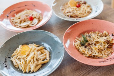Dishes from the chef of the restaurant. A dish on a table in a cafe. Appetizing food from the restaurant menu. Fresh and tasty food. Four types of pasta in plates on a wooden table