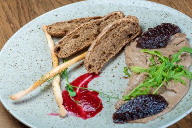 Dishes from the chef of the restaurant. A dish on a table in a cafe. Appetizing food from the restaurant menu. Fresh and tasty food. Pate with bread and sauce with greens on a plate