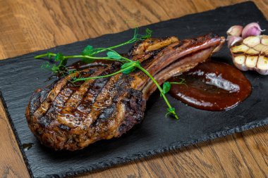 Dishes from the chef of the restaurant. A dish on a table in a cafe. Appetizing food from the restaurant menu. Fresh and tasty food. Grilled prime rib lies on a black board with sauce and a sprig of greens