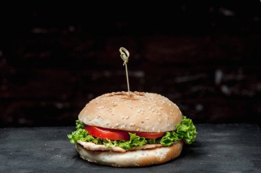 hamburger with a latch on a black board on a dark background. Delicious fast food. A product made by a chef in a cafe