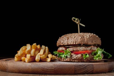 burger with a latch on a wooden board on a black background. Delicious fast food. A product made by a chef in a cafe