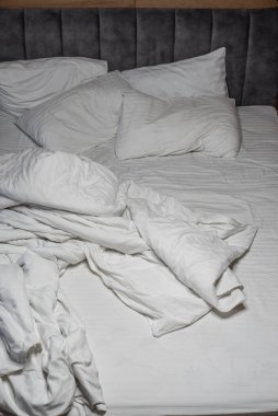 pillows and blankets lie on the bed in an improper form. unmade bedding on the bed. white bed linen