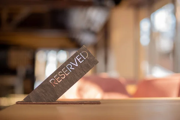 A sign indicating the reservation of a table by the client. A sign with the inscription Reserved on a table in a cafe. Wooden sign on the table.